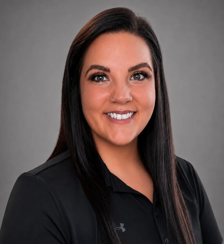 Savannah, BOC-certified athletic trainer, in a black polo against a teal studio backdrop